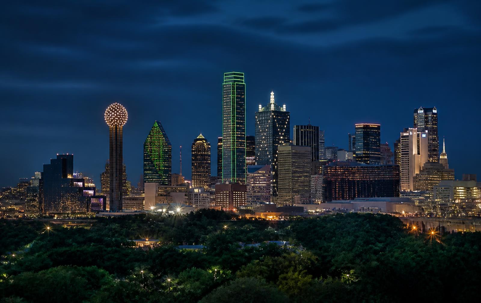 Dallas downtown skyline at blue hour beyond a tree-lined neighborhood